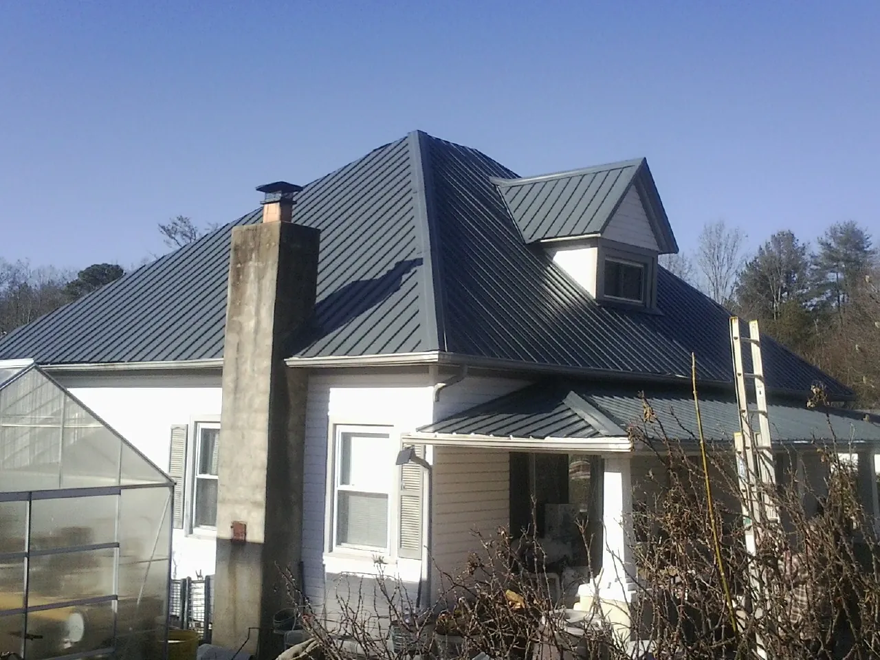 Dark blue standing seam metal roof on a white farmhouse with dormer — Slate & Tile Roof Repair by Roofing Brothers in Concord